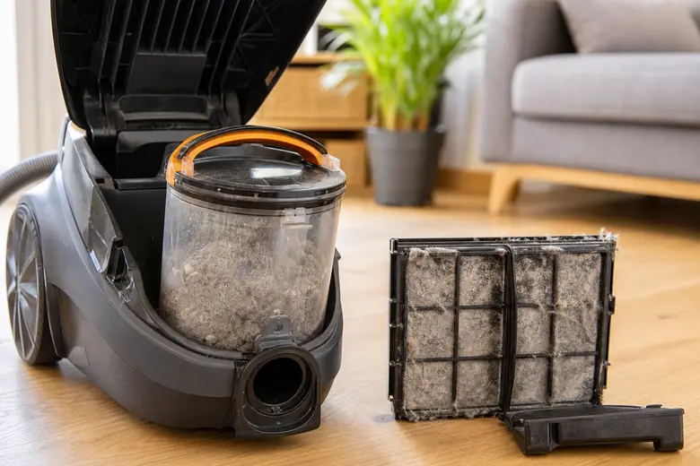 Réservoir d’aspirateur plein de poussière et filtre encrassé posés sur le sol d’un salon