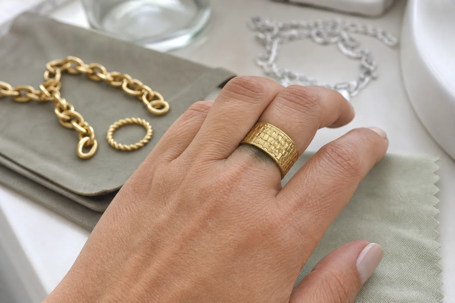 Main portant une bague fantaisie dorée, avec bracelets et chiffon de nettoyage posés à proximité