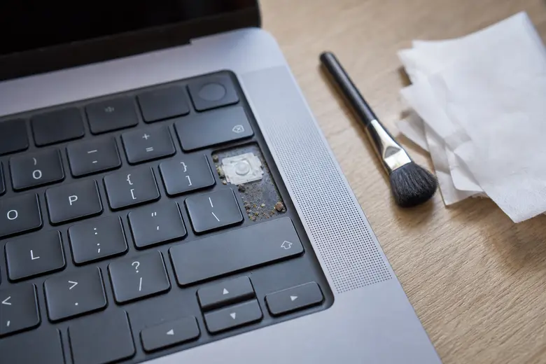 Touche de clavier d’ordinateur portable retirée, révélant de la poussière accumulée, avec un pinceau de nettoyage à proximité