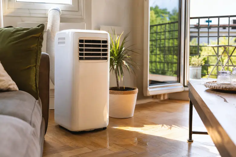 Climatiseur mobile blanc installé dans un salon lumineux, avec son tuyau d’évacuation raccordé à la fenêtre