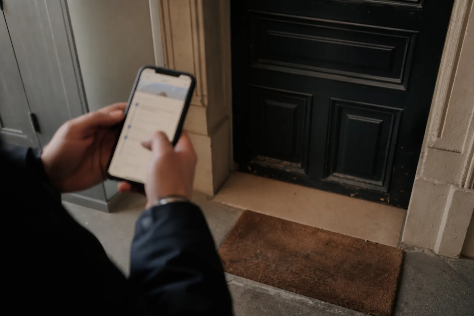 Seuil de porte d’un appartement sans colis, suivi de livraison consulté sur un smartphone