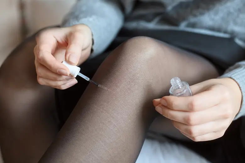Main appliquant du vernis à ongles transparent sur une maille filée d'un collant au niveau du genou