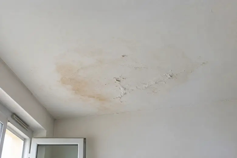 Tache d'humidité sur un plafond blanc avec de la peinture qui cloque, signe d'un dégât des eaux