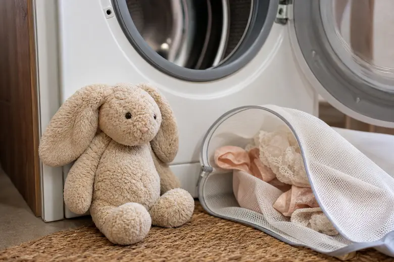 Peluche doudou posée à côté d’un filet à linge délicat devant un lave-linge ouvert