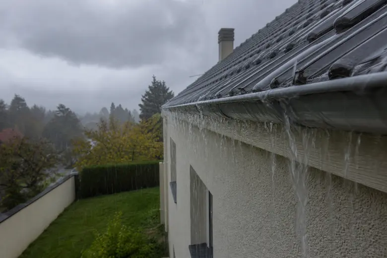 Gouttière de toiture qui déborde d'eau de pluie le long d'une façade pendant un orage