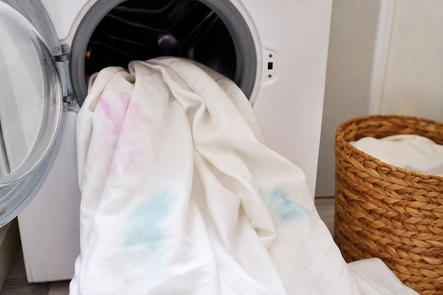 Housse de couette blanche sortant du lave-linge avec des traces de couleur déteintes visibles sur le tissu