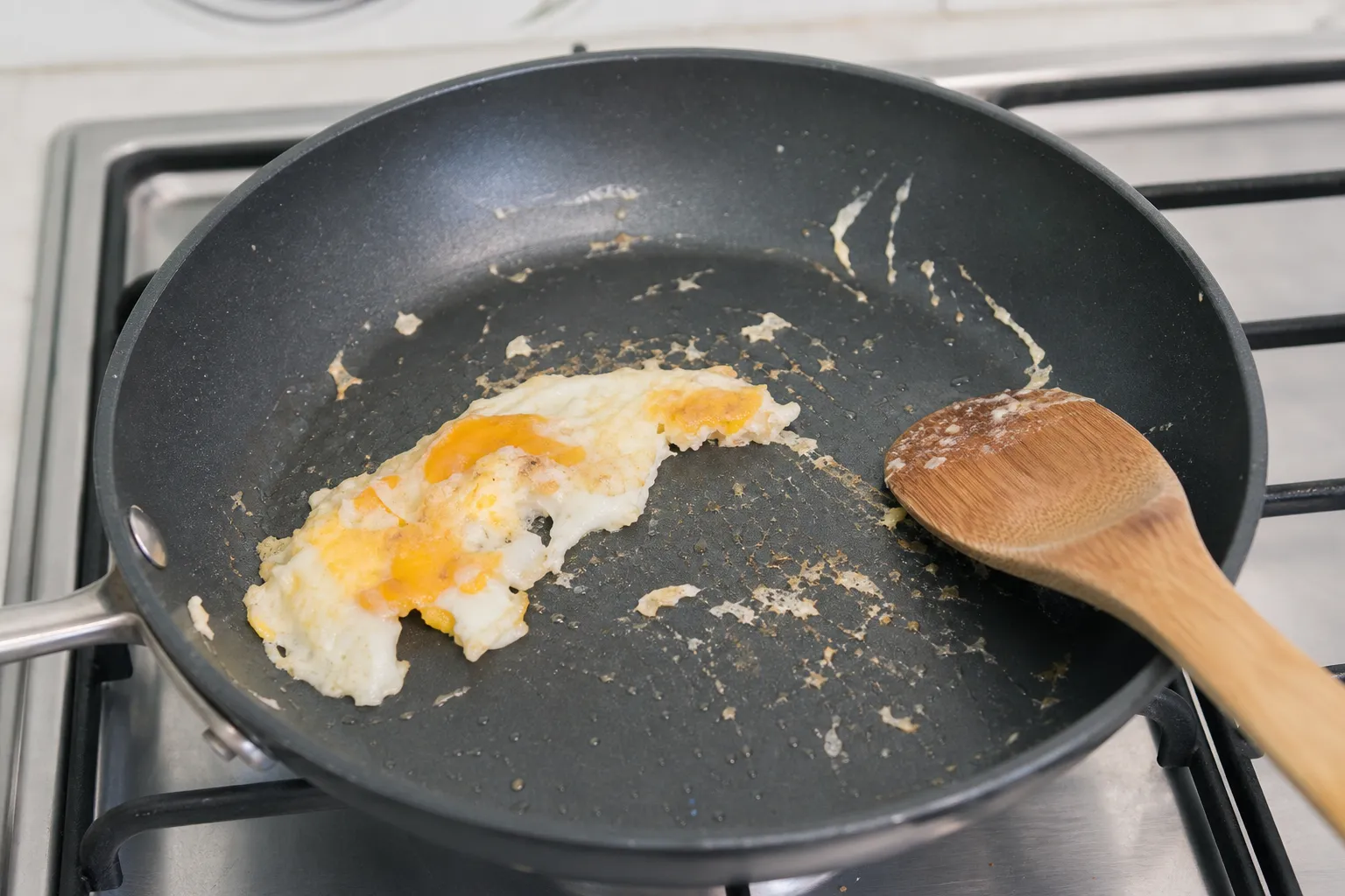 Œuf qui accroche dans une poêle antiadhésive sur une cuisinière, avec une spatule en bois posée à côté