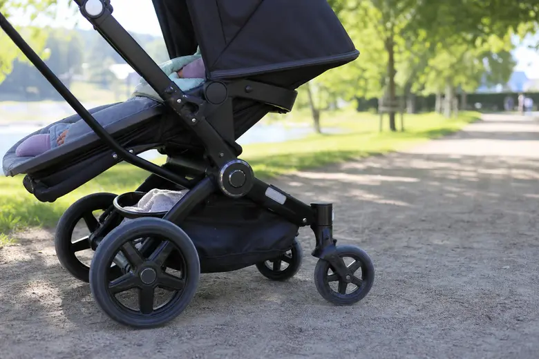 Poussette d’enfant vue de profil dans un parc, roues et châssis visibles