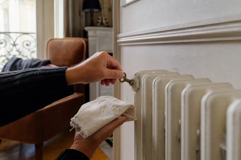 Personne purgeant un radiateur en fonte avec une clé de purge dans un salon