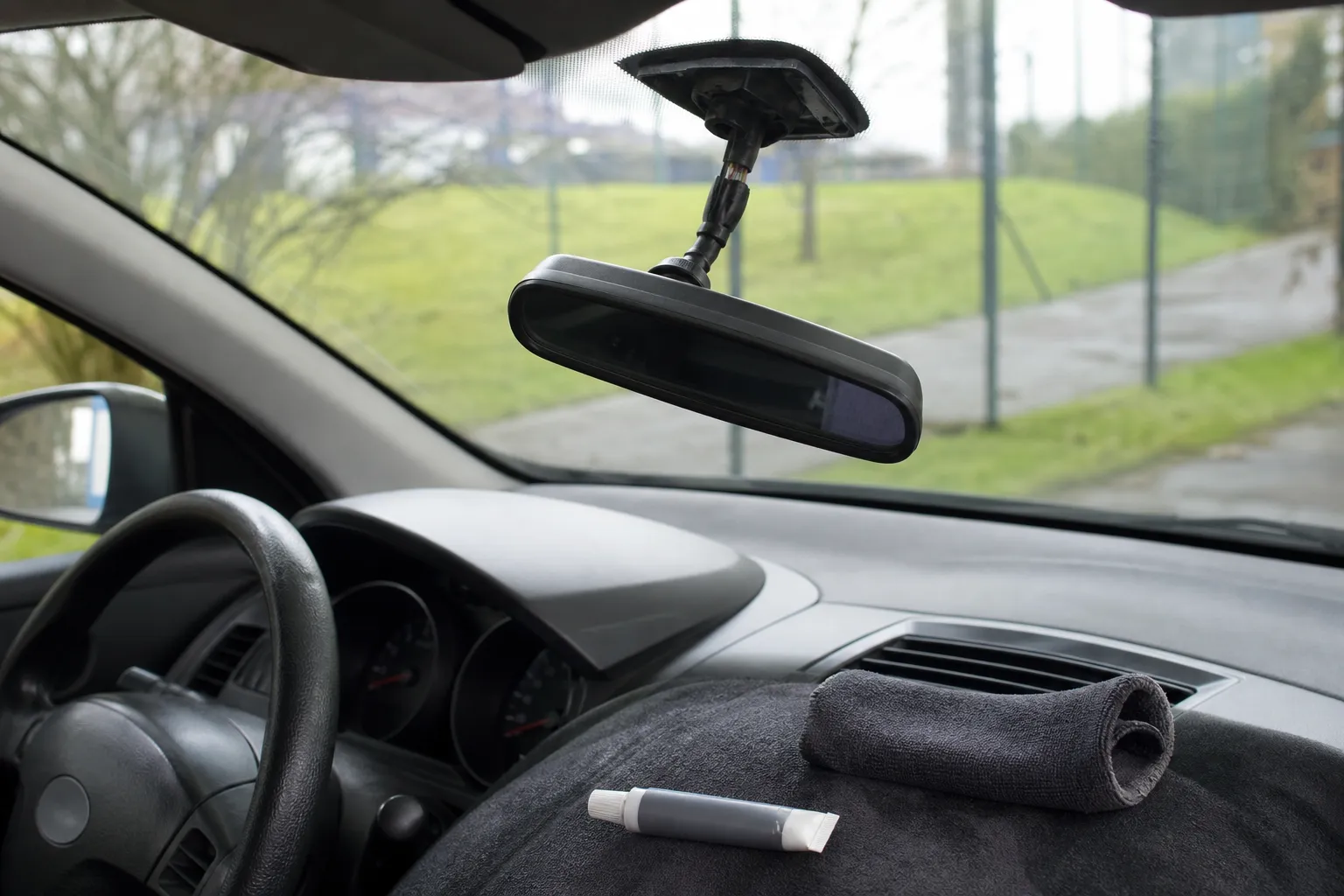 Rétroviseur intérieur de voiture partiellement décollé du pare-brise, avec un tube de colle et un chiffon posés sur le tableau de bord