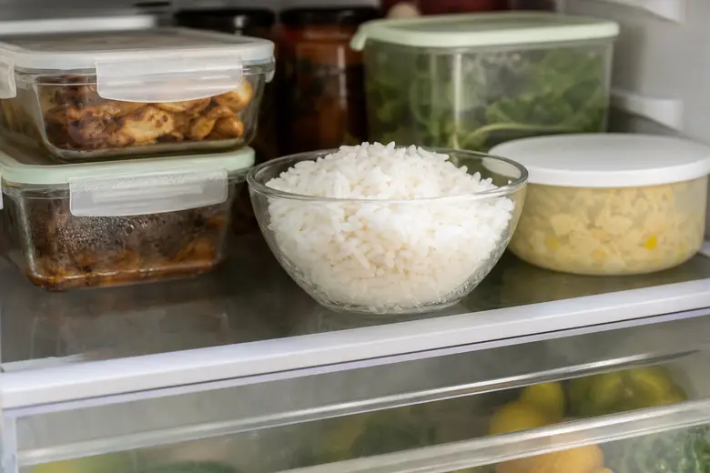 Bol de riz blanc cuit posé sur une étagère de réfrigérateur, à côté d'autres restes dans des contenants