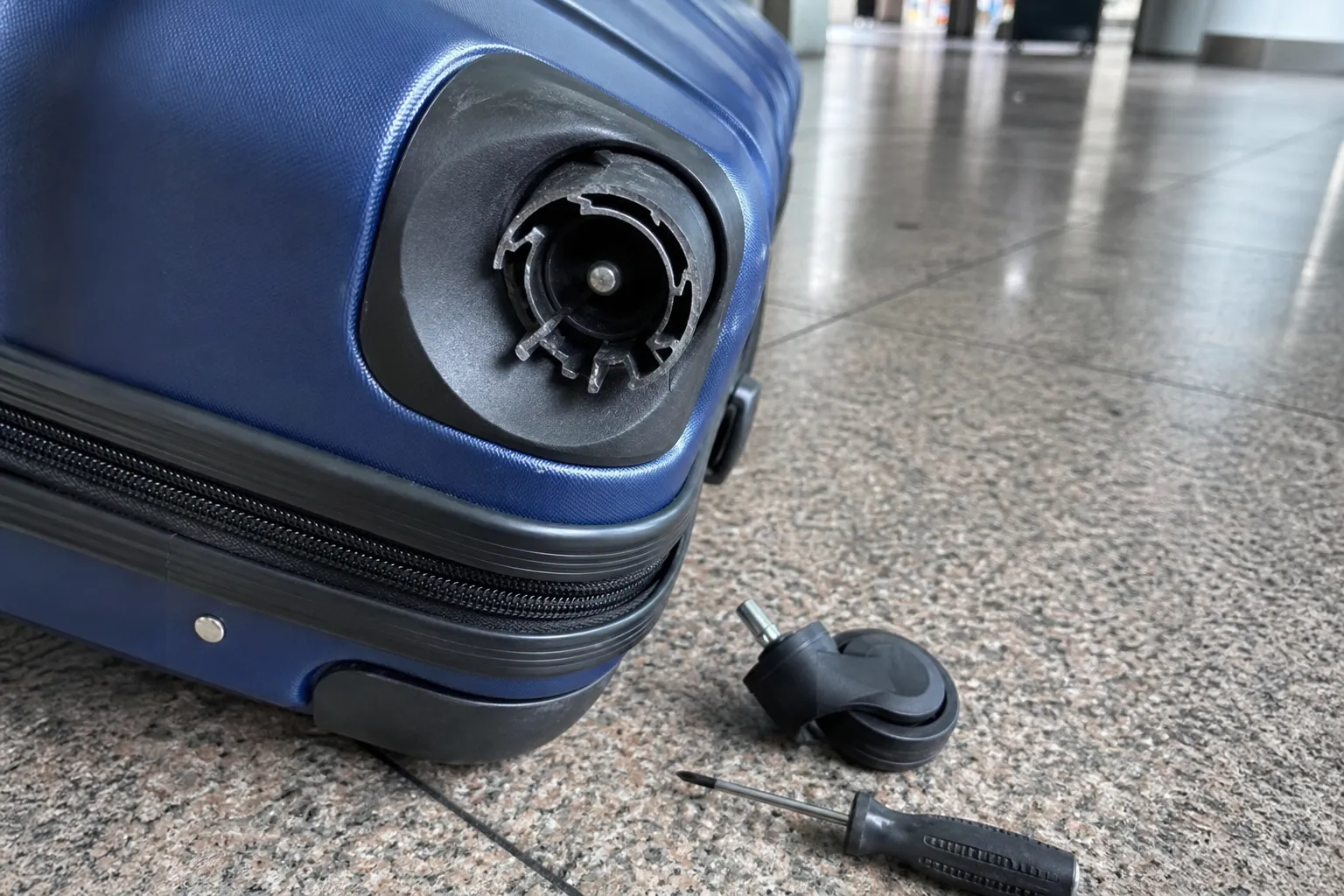 Roulette de valise cassée au sol à côté d’une roulette de rechange et d’un tournevis