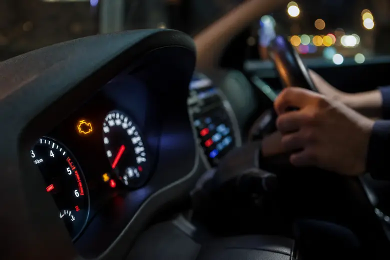Voyant moteur orange allumé sur le tableau de bord d’une voiture, mains du conducteur sur le volant